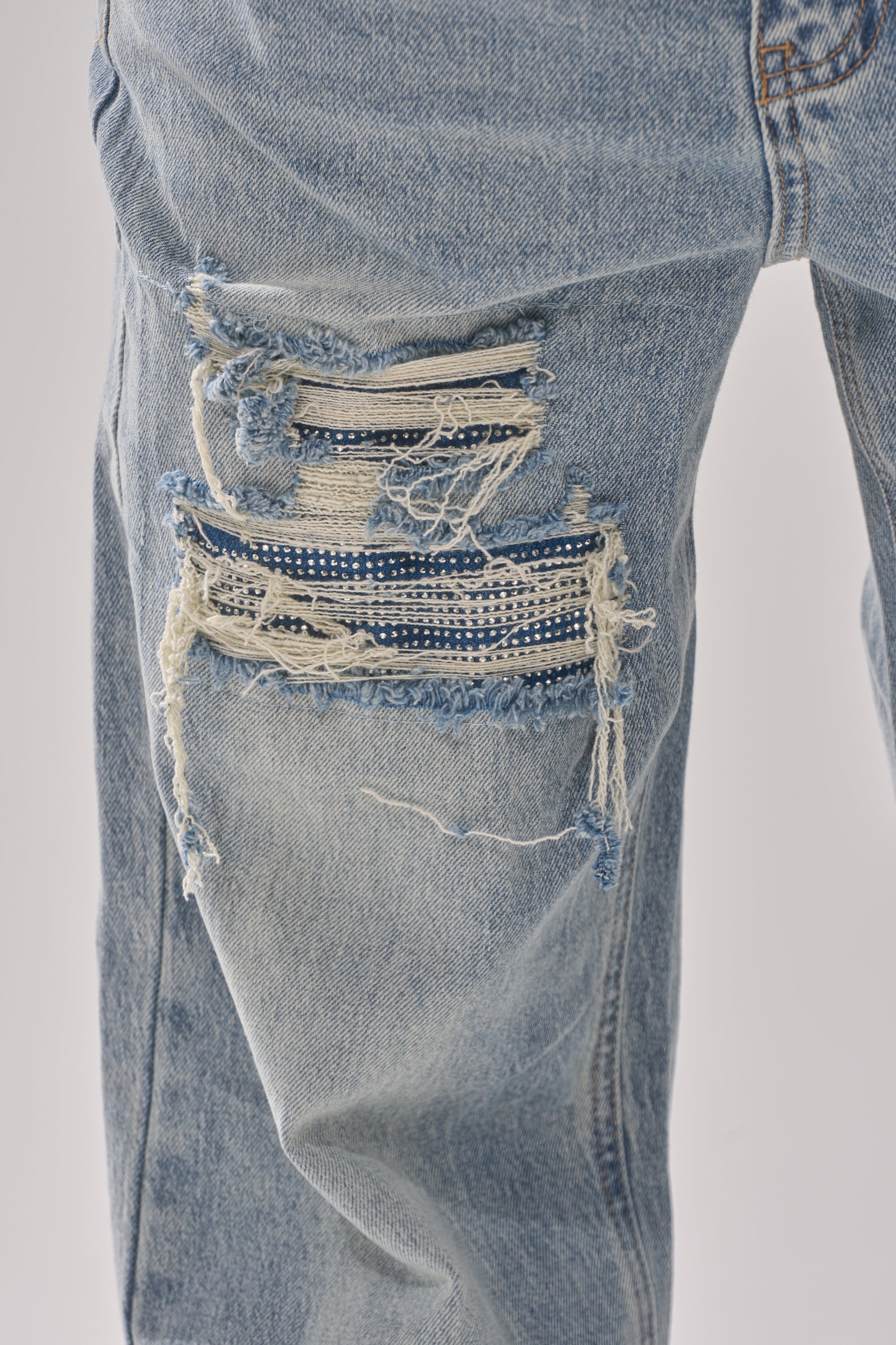 A close-up of the RUN AWAY WITH ME RELAXED DENIM high-rise jeans in light blue, featuring a large frayed rip on the thigh that reveals a blue and white checkered fabric patch beneath. 5