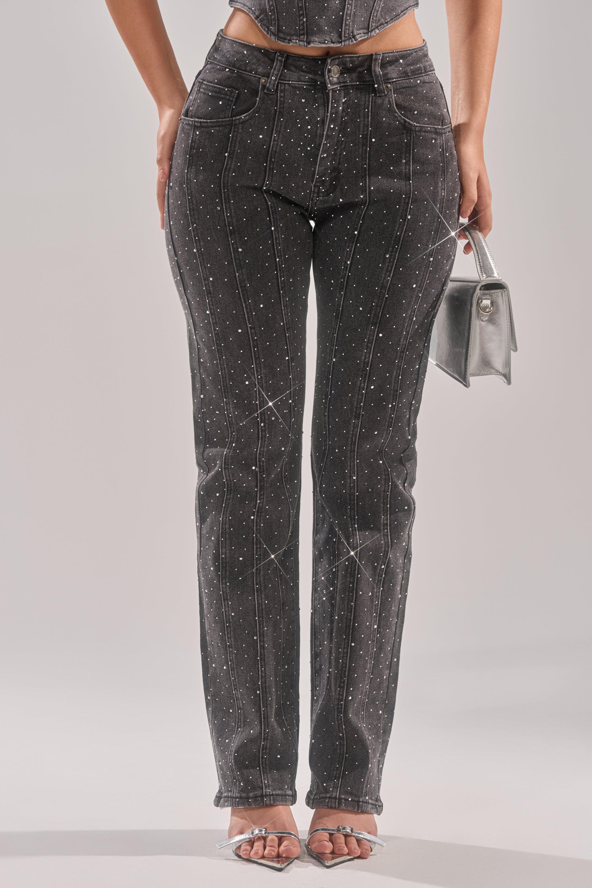 A person wearing LETS GET IT RELAXED DENIM PANT with rhinestones in a high rise relaxed fit, holding a silver handbag and pairing the look with clear heeled sandals. 2