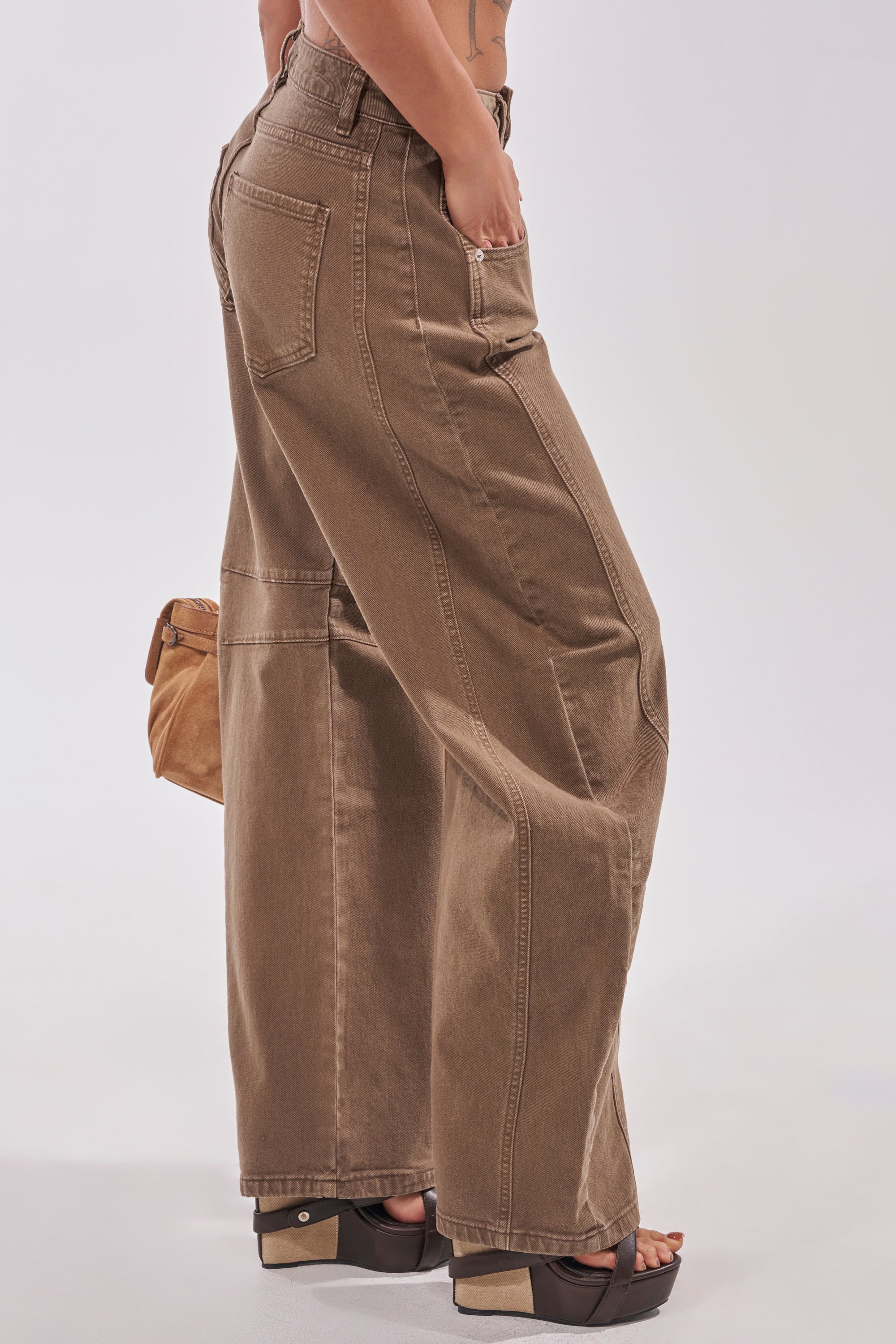 A person in high-waisted FEELING GREAT BARREL DENIM jeans and black platform sandals stands in a side pose, holding a tan handbag against a plain, light background. 3