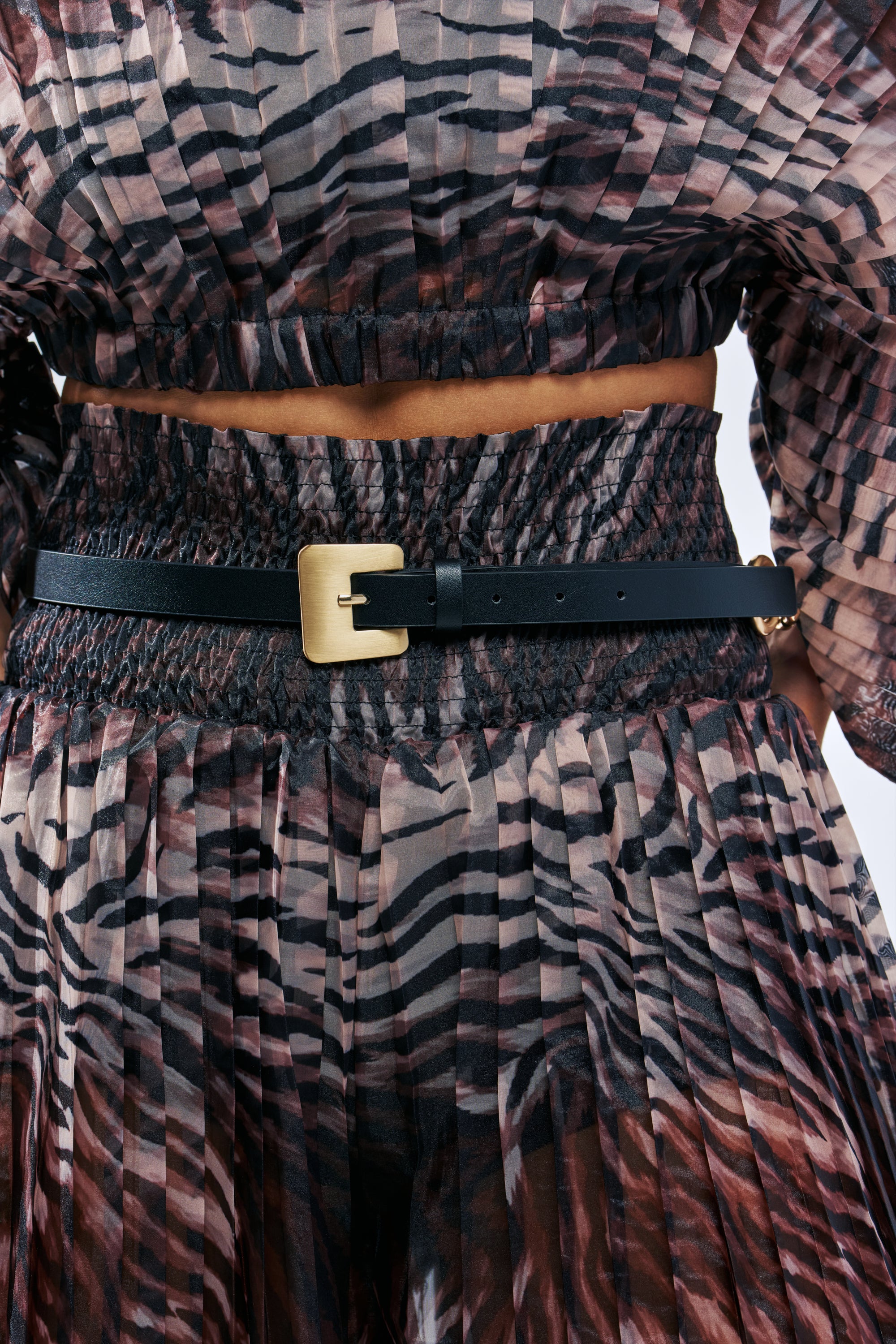 CHAINED 2 U SKINNY BELT in black faux leather with a gold square buckle, worn over a pleated tiger-print outfit.