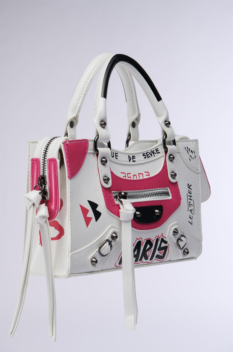 Introducing the PARIS LOVES ME GRAFFITI PURSE: a chic faux leather handbag featuring black and pink accents with Paris-inspired graphics. It boasts two handles, silver hardware, decorative zippers, and printed text and patterns for a modern, edgy appearance. 2