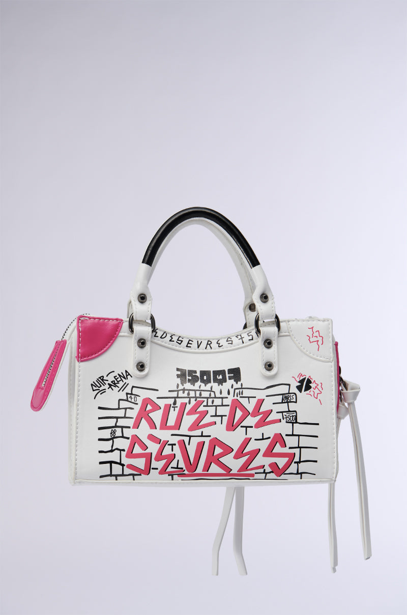 Introducing the PARIS LOVES ME GRAFFITI PURSE, a faux leather handbag adorned with black and pink graffiti-style designs. It features black handles, pink accents, and a playful pink tag. The bold text and geometric patterns capture a Parisian spirit against a brick wall backdrop.