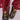 A person wearing transparent, red, loose-fitting pants stands with feet slightly apart, showcasing the AZALEA WANG QUINBY BROCADE CLOG IN BLACK. These black brocade mules feature colorful, intricate floral embroidery and a decorative buckle on each shoe against a plain, light-colored background.