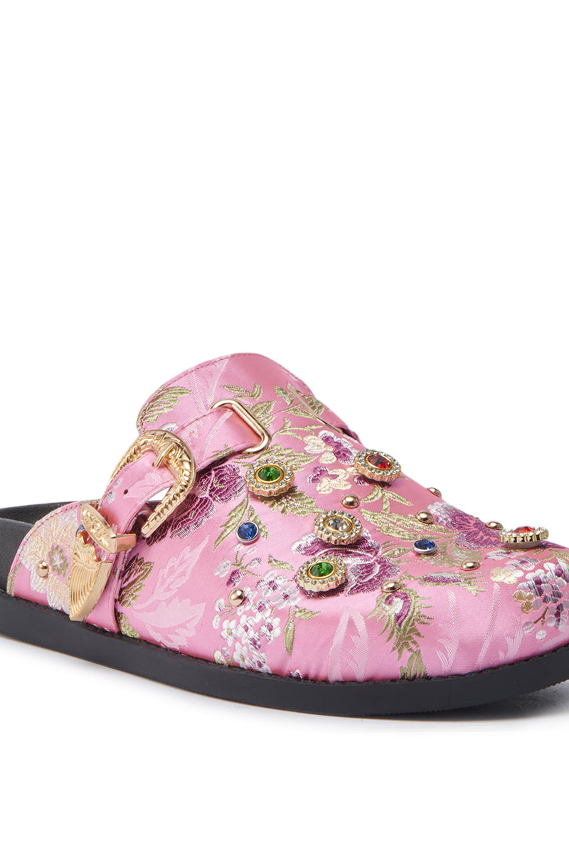 The AZALEA WANG QUINBY BROCADE CLOG IN PINK is a pink slip-on mule featuring floral embroidery, gemstone accents, a gold buckle, and colorful jeweled embellishments on a black sole.