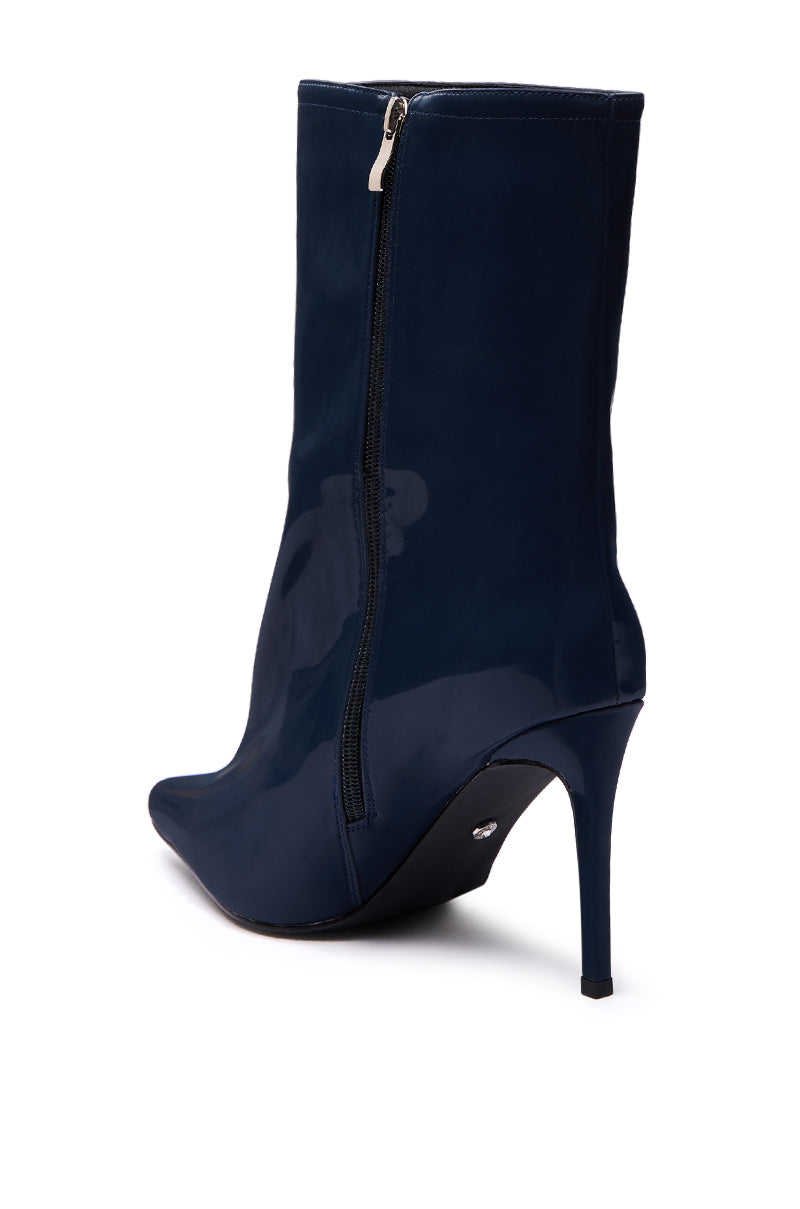 The AZALEA WANG QUINNTA NAVY BOOTIE features glossy faux patent leather, a pointed toe, stiletto heel, and side zipper, shown from a back angled view.