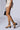 A person is wearing the AZALEA WANG QUINTON Black Chunky Sandal with a light-colored, ruffled mini skirt. They are also carrying a small, black textured handbag. The background is plain and neutral.