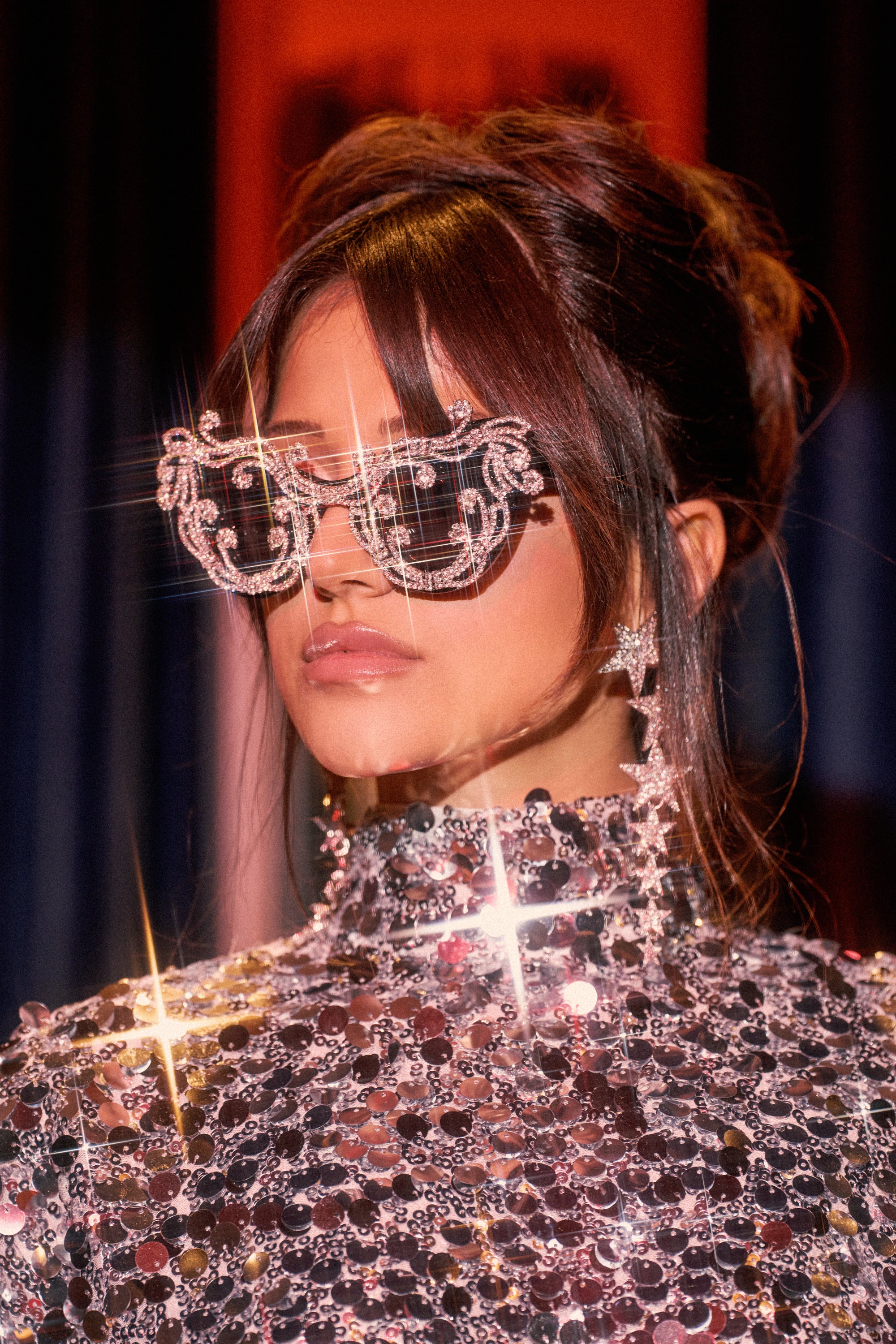 A woman wears OVER THE TOP SUNGLASSES with a sequin high-neck top, star-shaped earrings, glossy lips, and an updo. Light reflections add a sparkling effect.