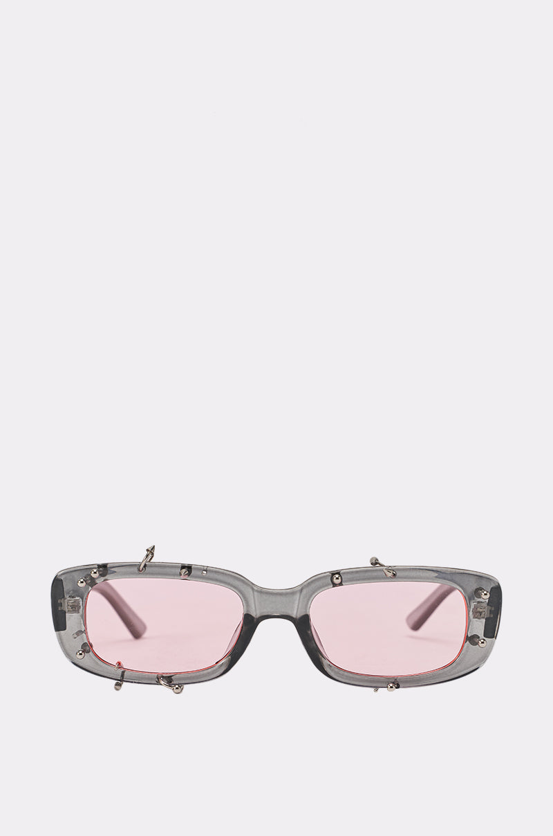 PIERCED THRU SUNGLASSES feature rectangular translucent gray frames with metallic accents and pink-tinted lenses, shown against a plain light background. 1