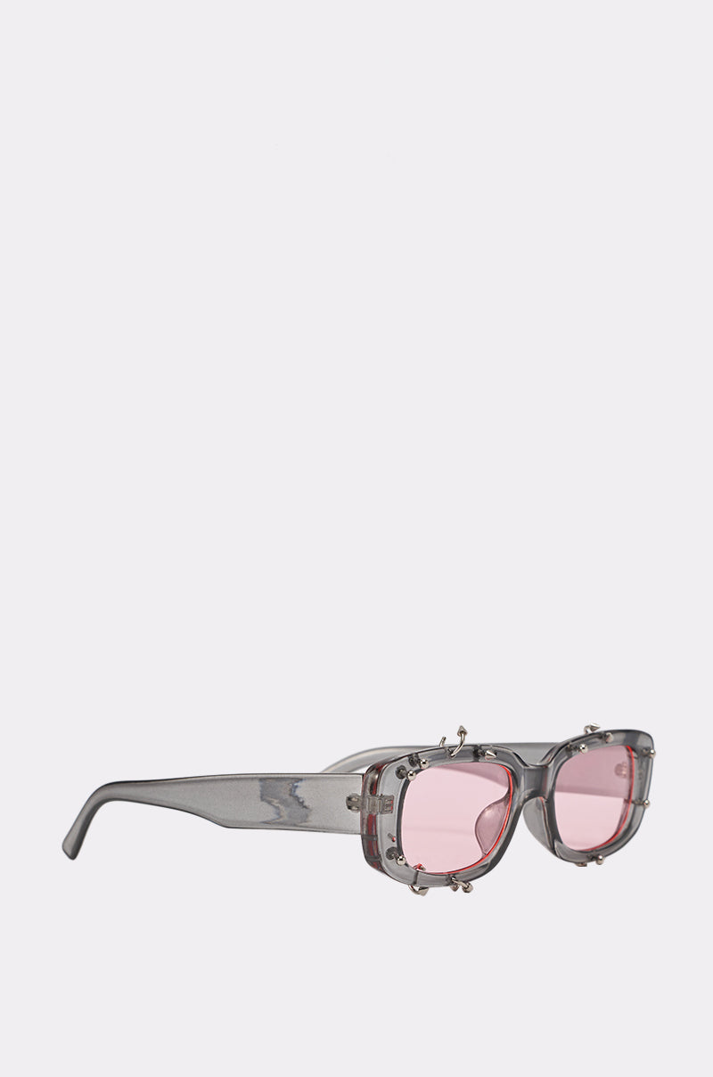 PIERCED THRU SUNGLASSES: Gray translucent streetwear frames with rectangular, pink-tinted lenses and metallic accents, shown on a plain white background. 2