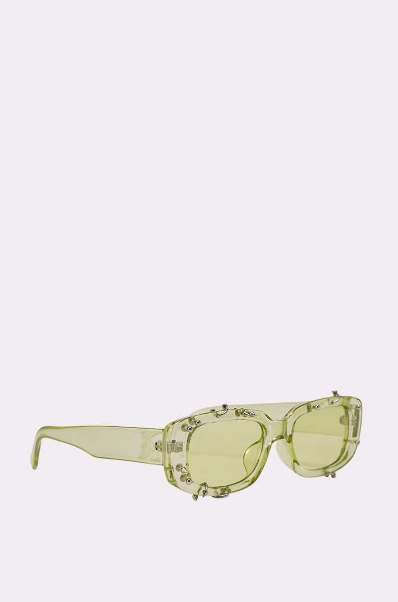 WITH A TWIST SUNGLASSES feature light green translucent rectangular lenses, bold thick frames, and decorative metallic studs on the front, shown on a plain white background. 3