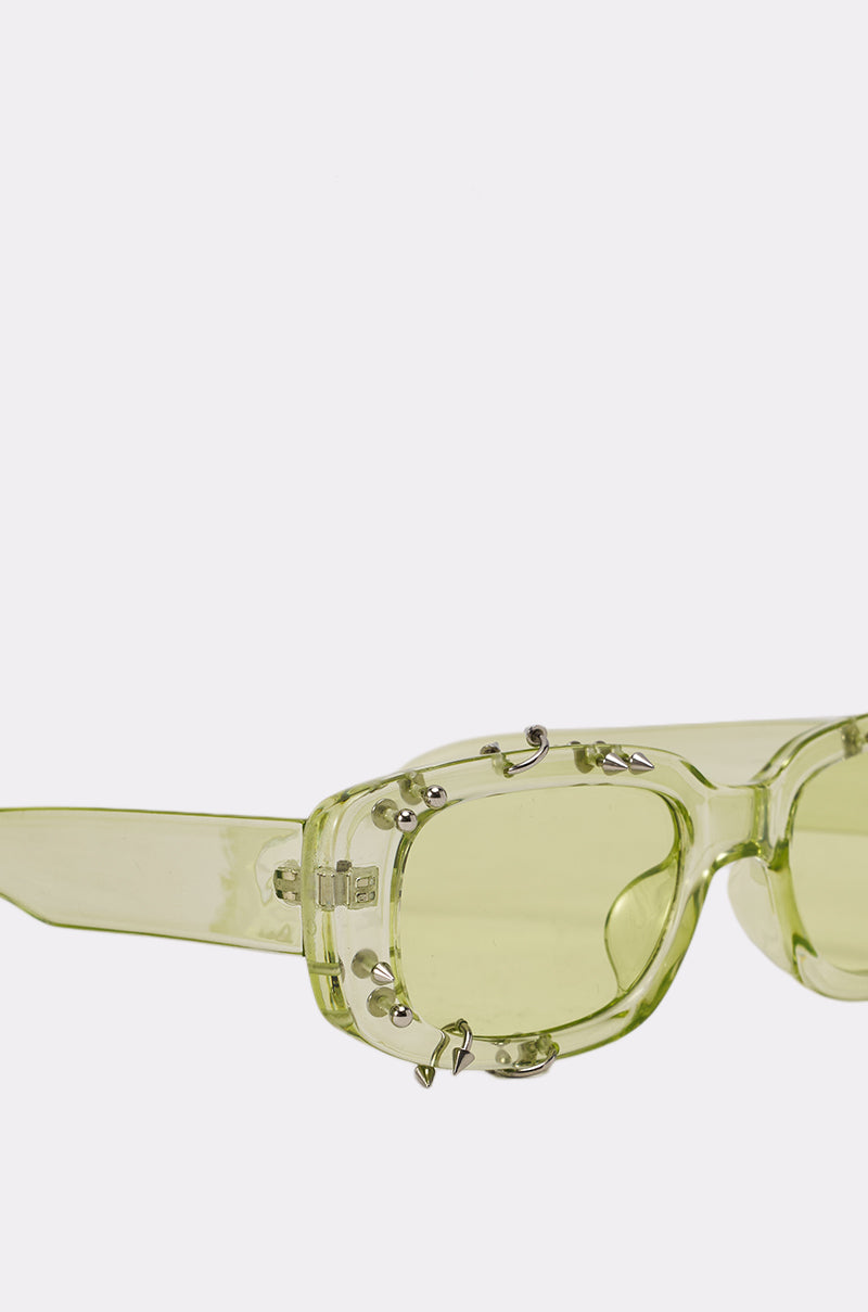 WITH A TWIST SUNGLASSES: Stylish, translucent green rectangular frames with silver decorative studs and pierced details, showcased against a plain white background. 4