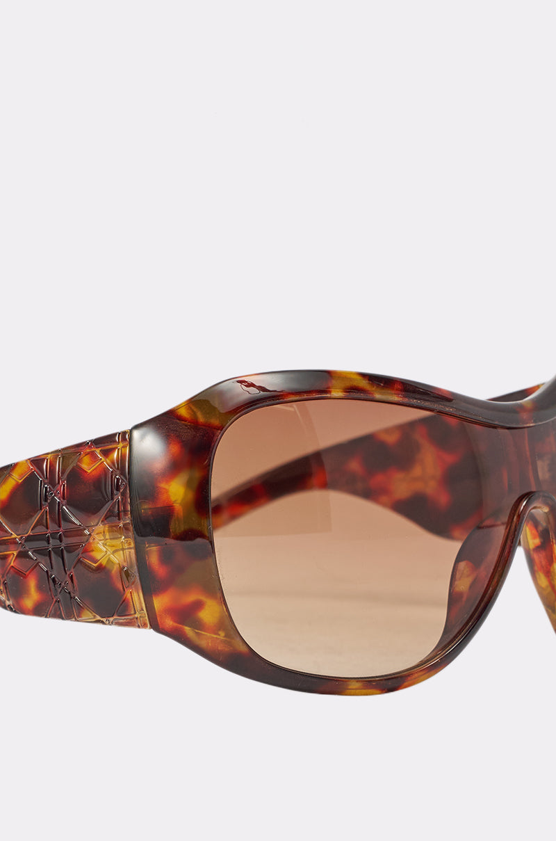Close-up of TORTALLY SUNGLASSES featuring a brown tortoise shell frame, geometric wide arms, and brown-tinted lenses against a light background. 4