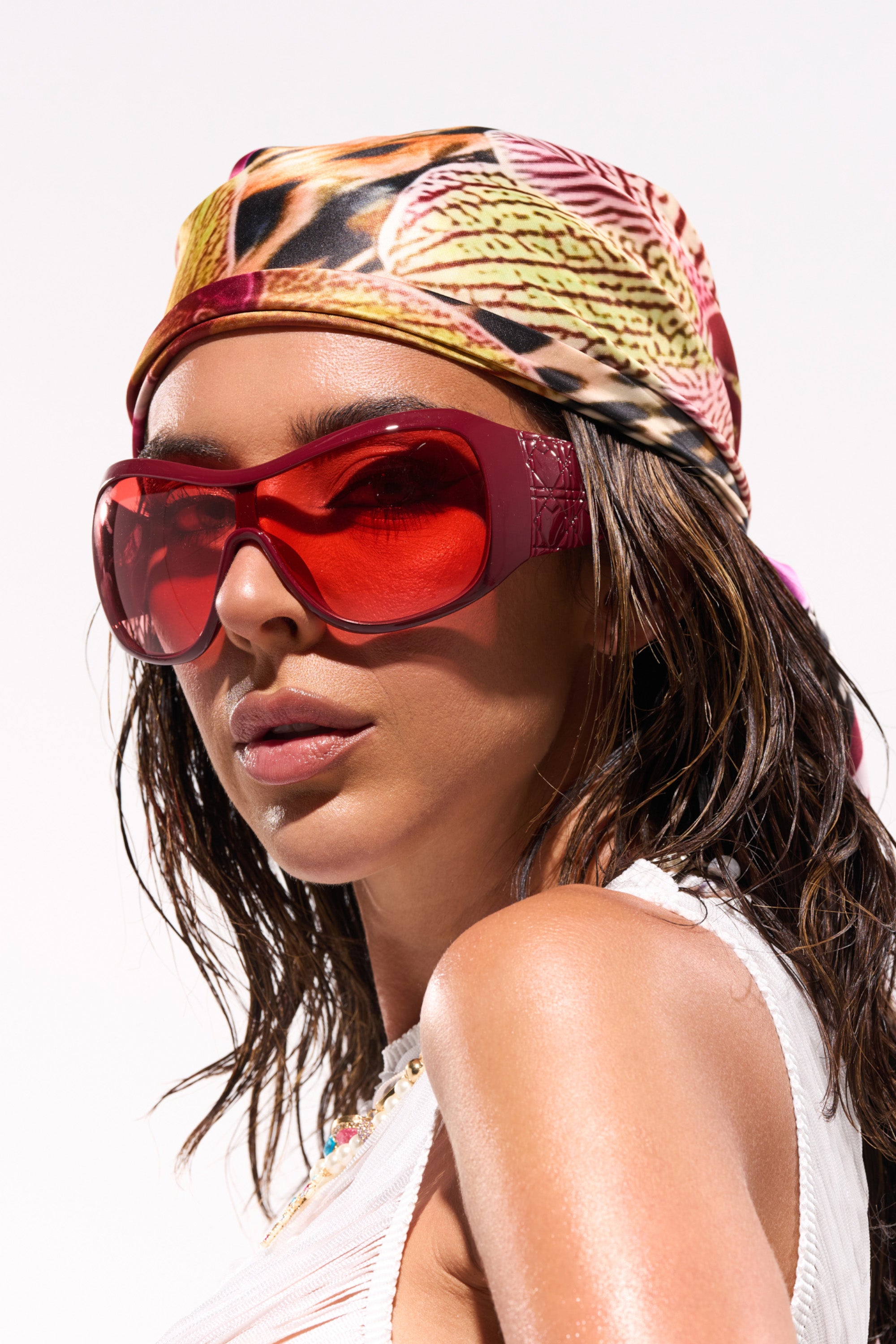 A woman with wet hair wears the WITH LUV SUNGLASSES, a colorful patterned headscarf, and a white sleeveless top, gazing confidently at the camera against a plain light background. 0