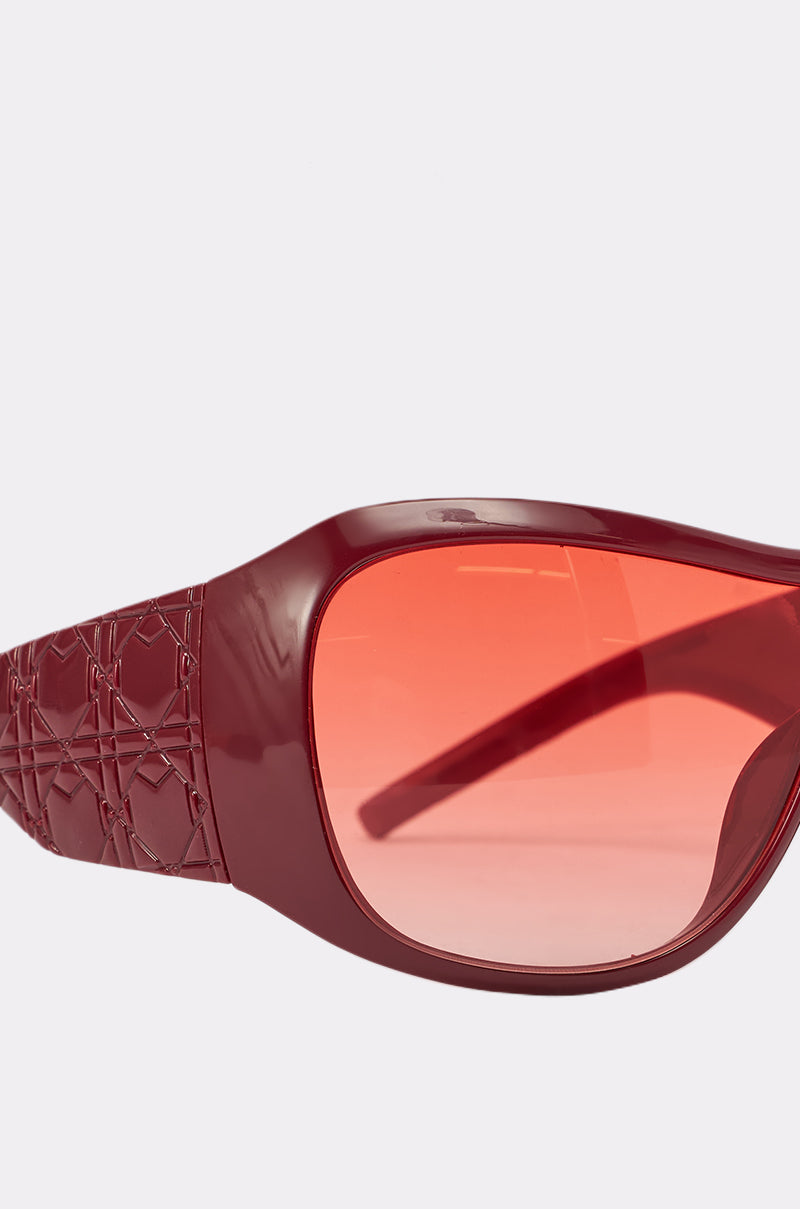 Close-up of WITH LUV SUNGLASSES featuring oversized maroon frames, textured patterned arms, and large red-tinted lenses set against a plain light background. 3