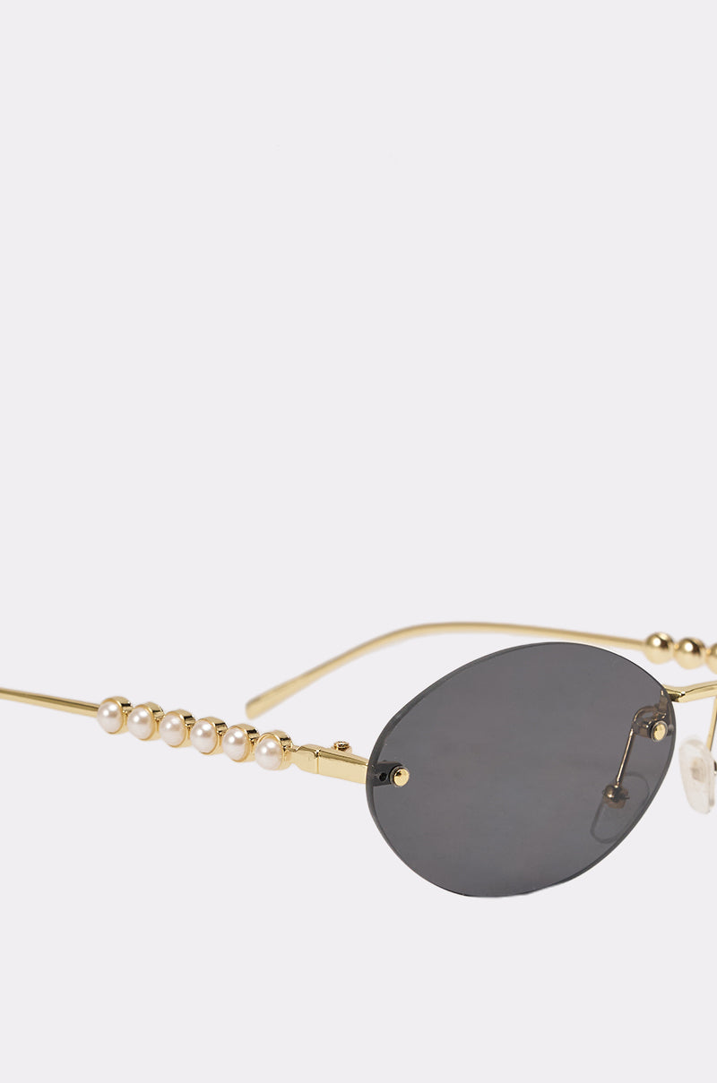 A close-up of SEE YA SUNGLASSES featuring vintage mini oval gold frames, black lenses, and pearl-decorated arms, set against a plain light background. 3