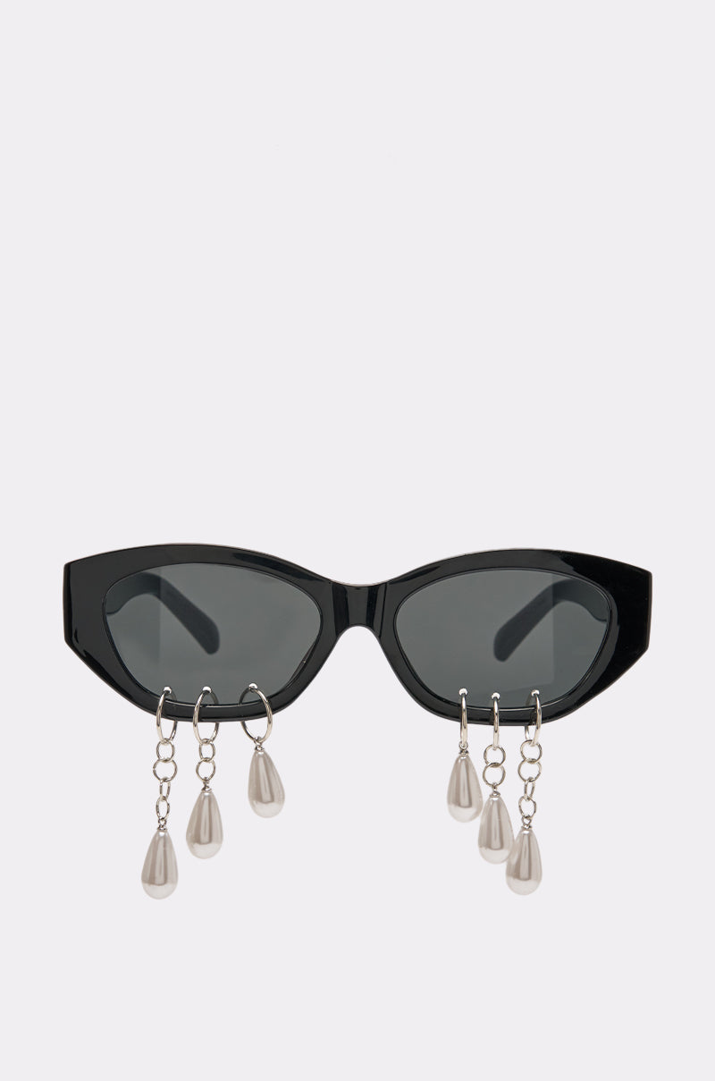 The PEARL TEARS SUNGLASSES feature bold black cat-eye frames adorned with pearl-like charms that dangle from short silver chains attached to the lower rims, making a striking statement against a plain white background.