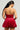 A woman with long black hair styled in a ponytail is wearing the THIS MOMENT VELVET ROMPER IN RED. She is facing away from the camera, accentuating the chic flare of the holiday ensemble's bubble silhouette.