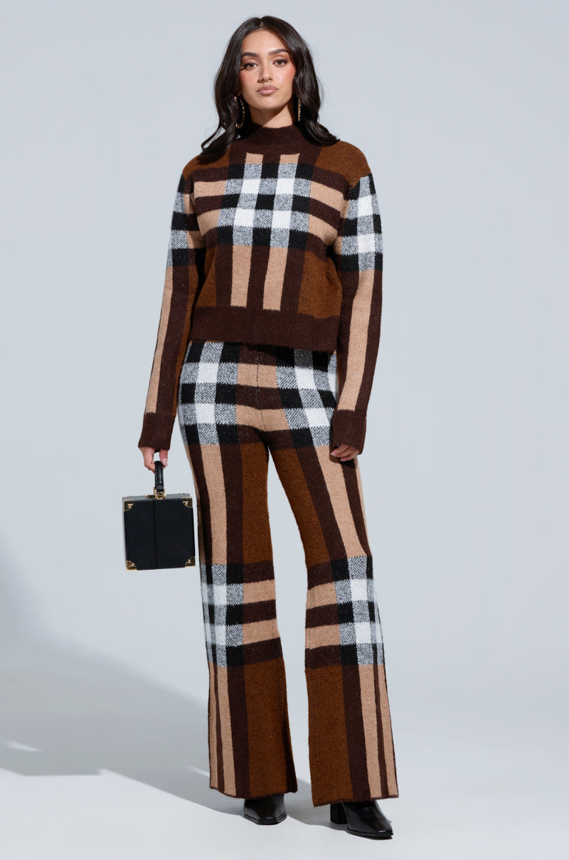 Against a simple backdrop, a woman showcases the ELISE PLAID KNIT PANT featuring a striking combination of brown, black, and white in a stylish ensemble. She accessorizes with an elegant black handbag and finishes her look with sleek black boots. 4
