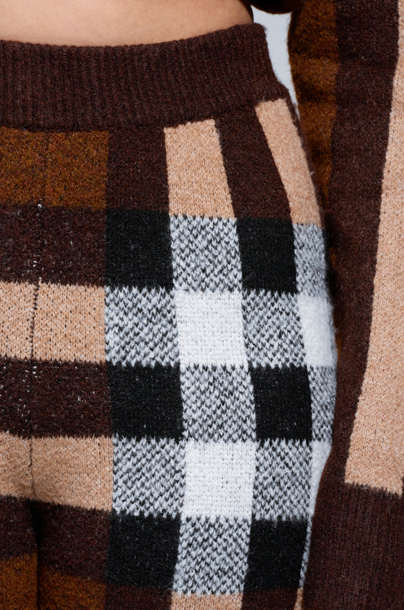 Close-up of a person wearing a checkered knitted top paired with the ELISE PLAID KNIT PANT. The design features squares in shades of brown, beige, black, and white. The texture appears soft and inviting for cooler days. 5