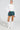 A person wearing the Sydney Fur Cuff Sweater in ivory, featuring oversized faux fur cuffs, paired with a green plaid skirt and knee-high white boots. They stand with one hand on their hip against a plain background.
