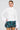 Wearing the SYDNEY FUR CUFF SWEATER IN IVORY, a woman with oversized faux fur cuffs and a plaid ruffled skirt strikes a confident pose against a plain gray background, her hand resting on her hip as she gazes at the camera.