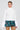 A person is wearing the Sydney Fur Cuff Sweater in ivory, which has an oversized fit and faux fur cuffs, paired with a green plaid skirt. They accessorize with long earrings and have slicked-back hair, standing against a plain background.
