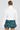 A person with their hair in a bun is wearing the Sydney Fur Cuff Sweater in ivory and a green plaid skirt. They are standing with their back to the camera against a plain background.