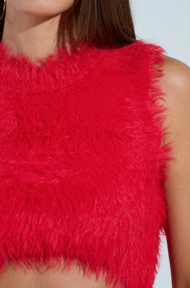 A person wears the SHAGGY RED CROP TOP, showcasing its fluffy texture and vibrant red hue. Their shoulder and long brown hair are visible against a light blue background, creating a perfect winter fashion look.