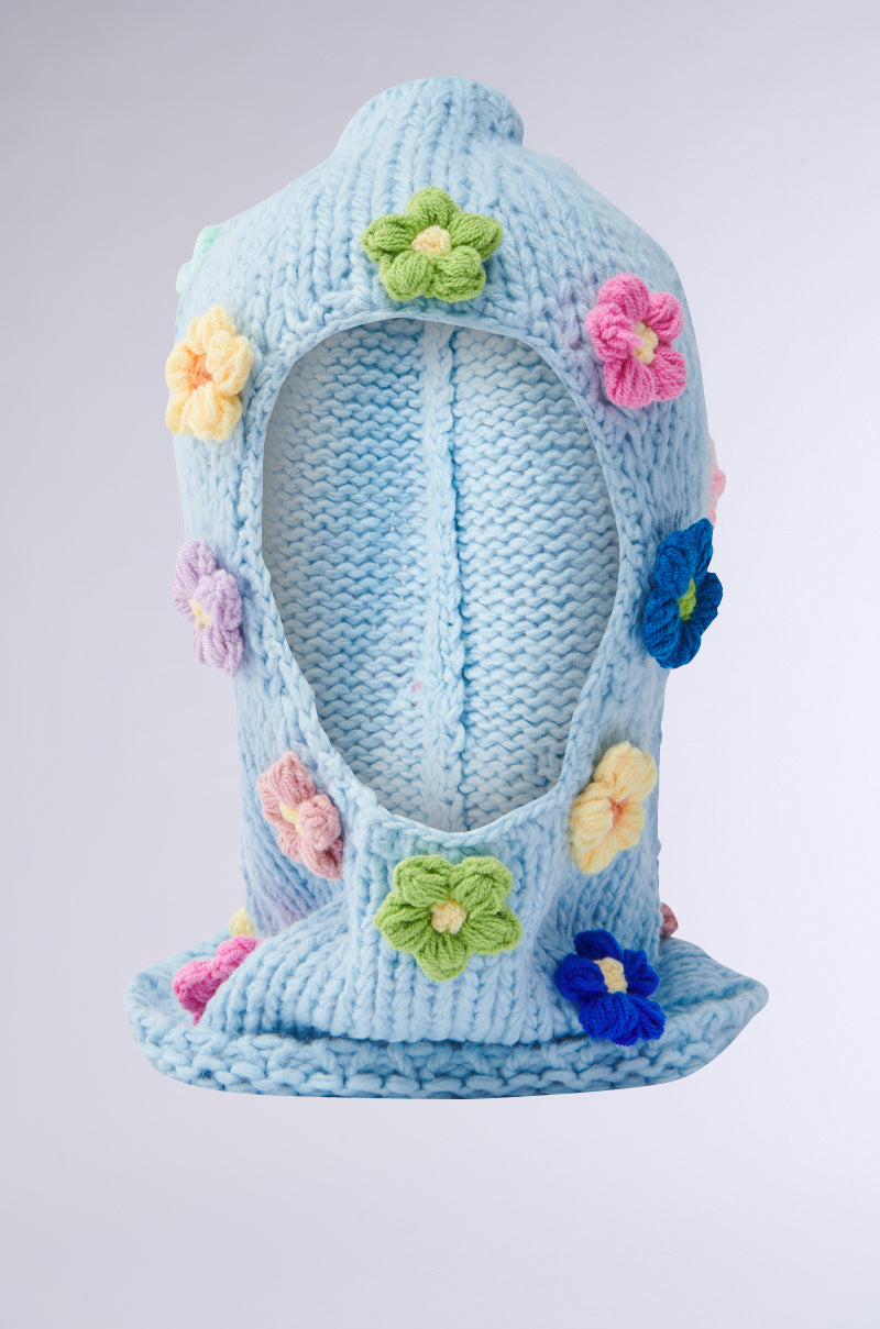 Meet the Bella Flower Balaclava: a cozy, light blue knit with crochet flower appliqués in pink, yellow, green, and blue pastels and brights. It offers an open face area and a slightly slouched design for a snug yet stylish fit. 2