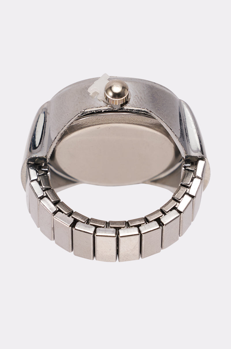 A close-up of the ITS TIME RING, a silver metallic accessory wristwatch with a linked band, shown from the back with winding crown and clasp visible; watch face is hidden. 3