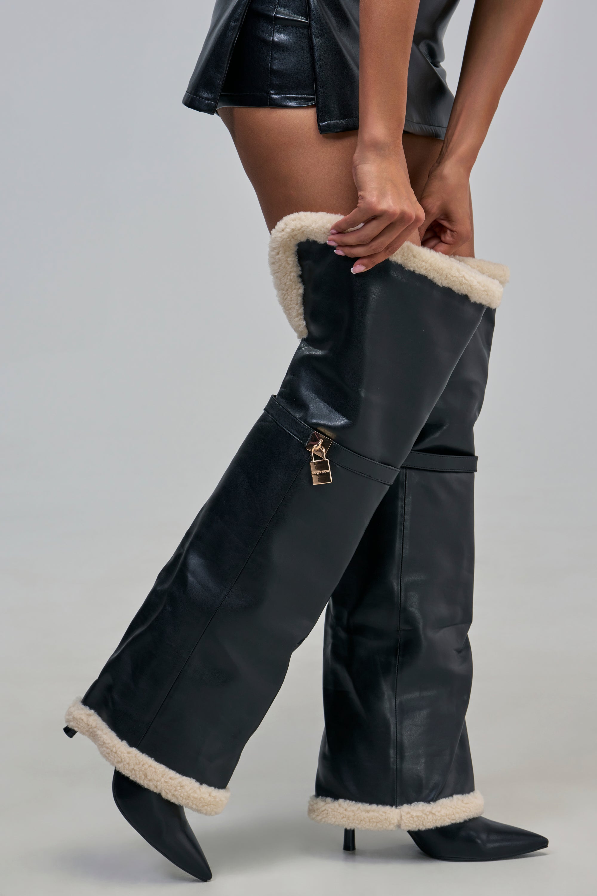 AZALEA WANG RACHANA BLACK PU AND SHERPA STILETTO BOOT in black faux leather with thigh-high length, white faux-shearling trim, and a small gold padlock detail on the side.