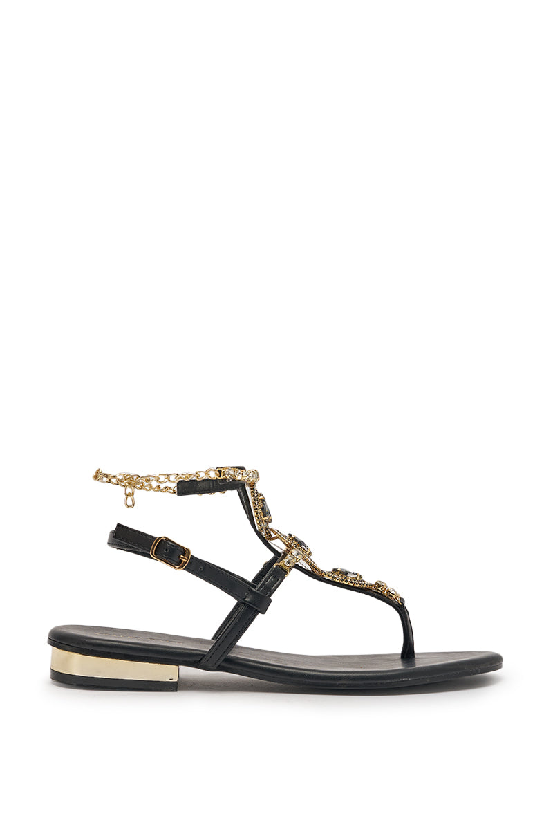 The AZALEA WANG RAFEE Black Rhinestone Embellished Flat Strap Sandal features black faux leather, gold accents, an ankle strap, a toe loop, rhinestone and jeweled embellishments, a gold chain detail, and a metallic gold low heel. 4