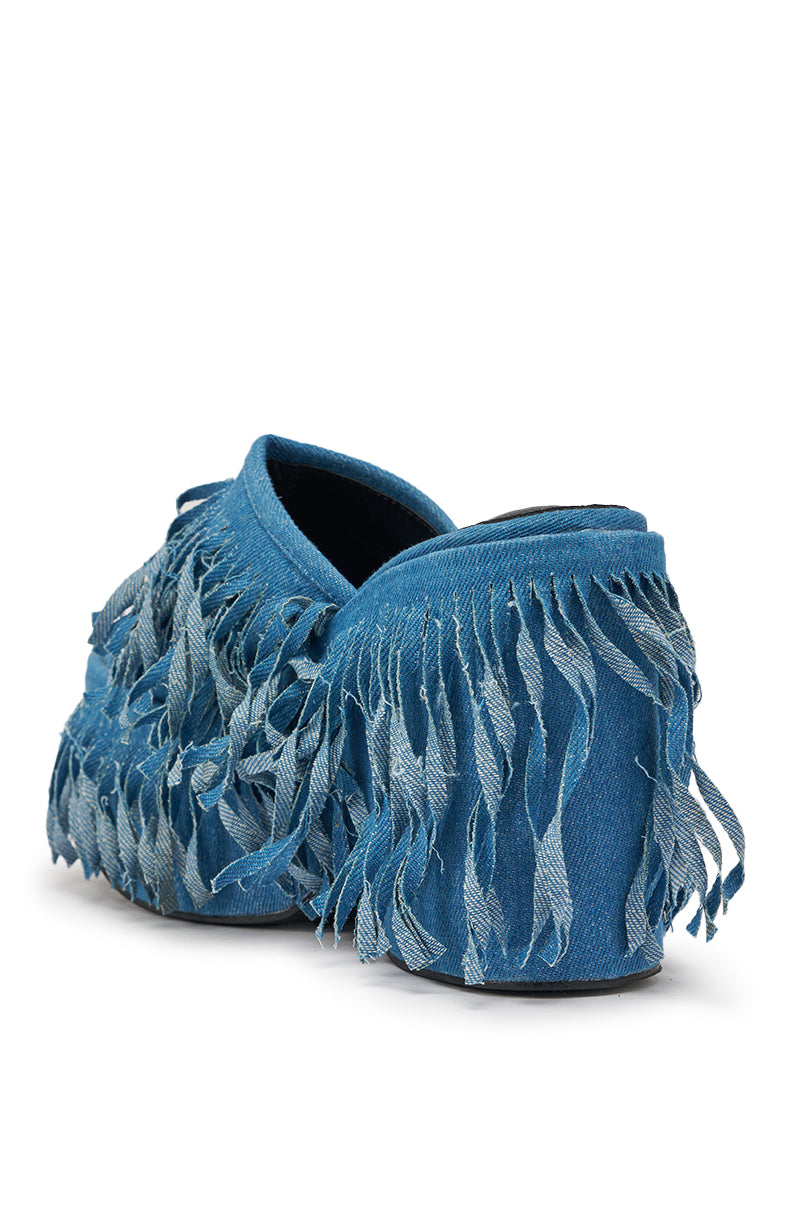 The AKIRA GOLD RAMESHA DENIM FRINGE PLATFORM SANDAL features blue denim slip-on style with fringe trim covering the upper and sides, shown from the back and slightly to the side. 5