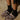 A person stands on a textured surface, featuring the AZALEA WANG RAMIE LEOPARD MULE FLAT slippers adorned with faux fur uppers and black straps over black socks. A fringe detail enhances the top of the image, adding a stylish touch.