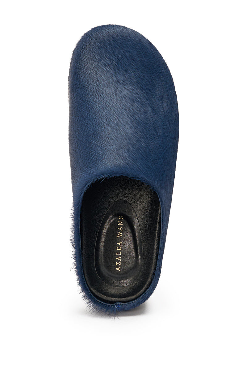 The AZALEA WANG RAMSES NAVY SLIP ON FLAT is a navy faux fur mule with a rounded toe, black insole, and "AZALEA WANG" gold text on the footbed, shown against a white background. 2