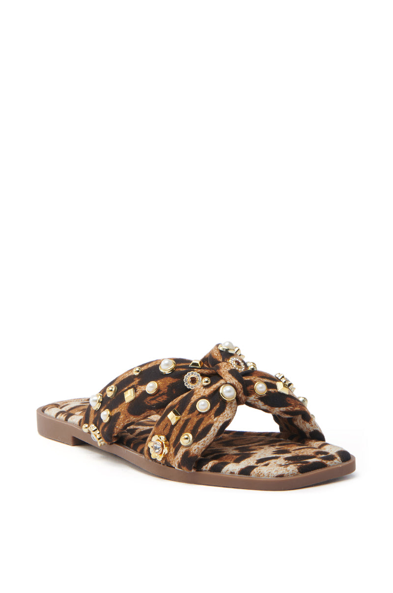 Step into luxury with the AKIRA RAMSEY LEOPARD FLAT SANDAL. Featuring crisscross straps embellished with gold and pearls, a cushioned insole, and a brown sole, these chic sandals offer leopard print style and ultimate comfort.