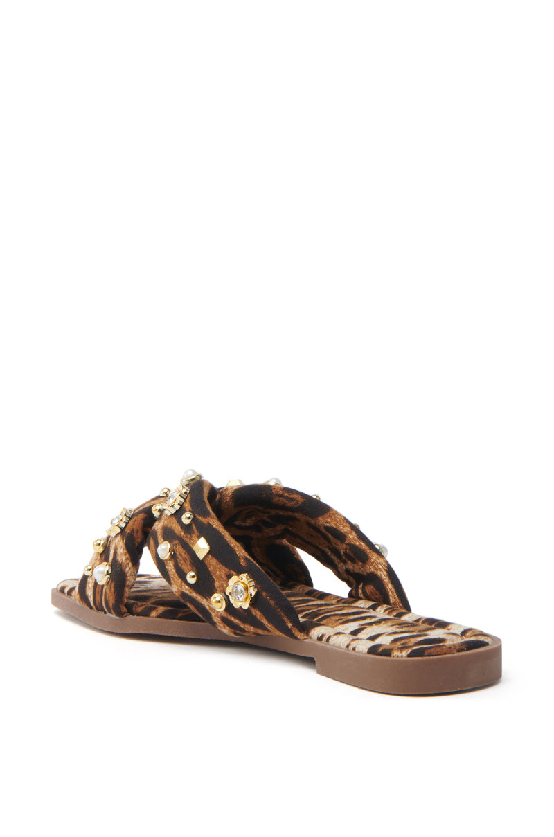 The AKIRA RAMSEY LEOPARD FLAT SANDAL features a brown sole, cushioned insole, and crisscross straps with a luxe leopard print and rhinestone embellishments for added sparkle.