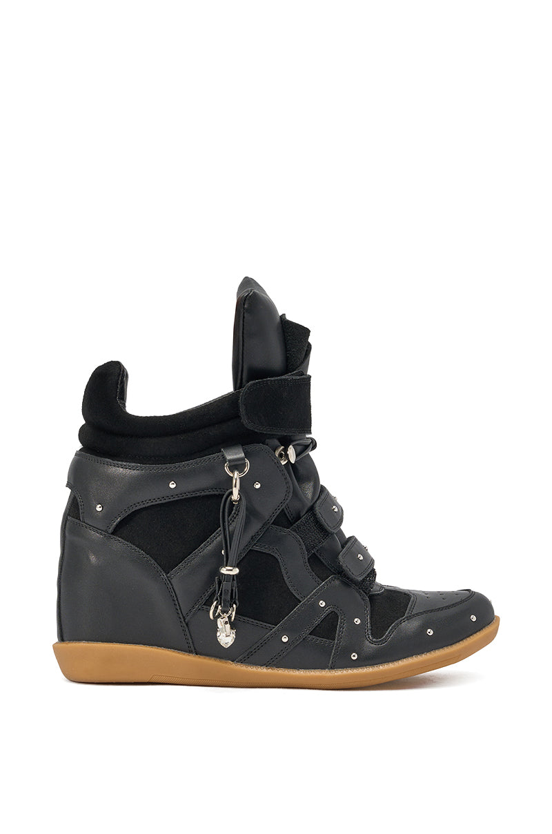 The AKIRA GOLD RANGELEY BLACK SILVER HARDWARE EMBELLISHED WEDGE SNEAKER features black faux leather and suede panels, silver studs, a chunky gum sole, and a side chain with skull charm, photographed against a white background. 2