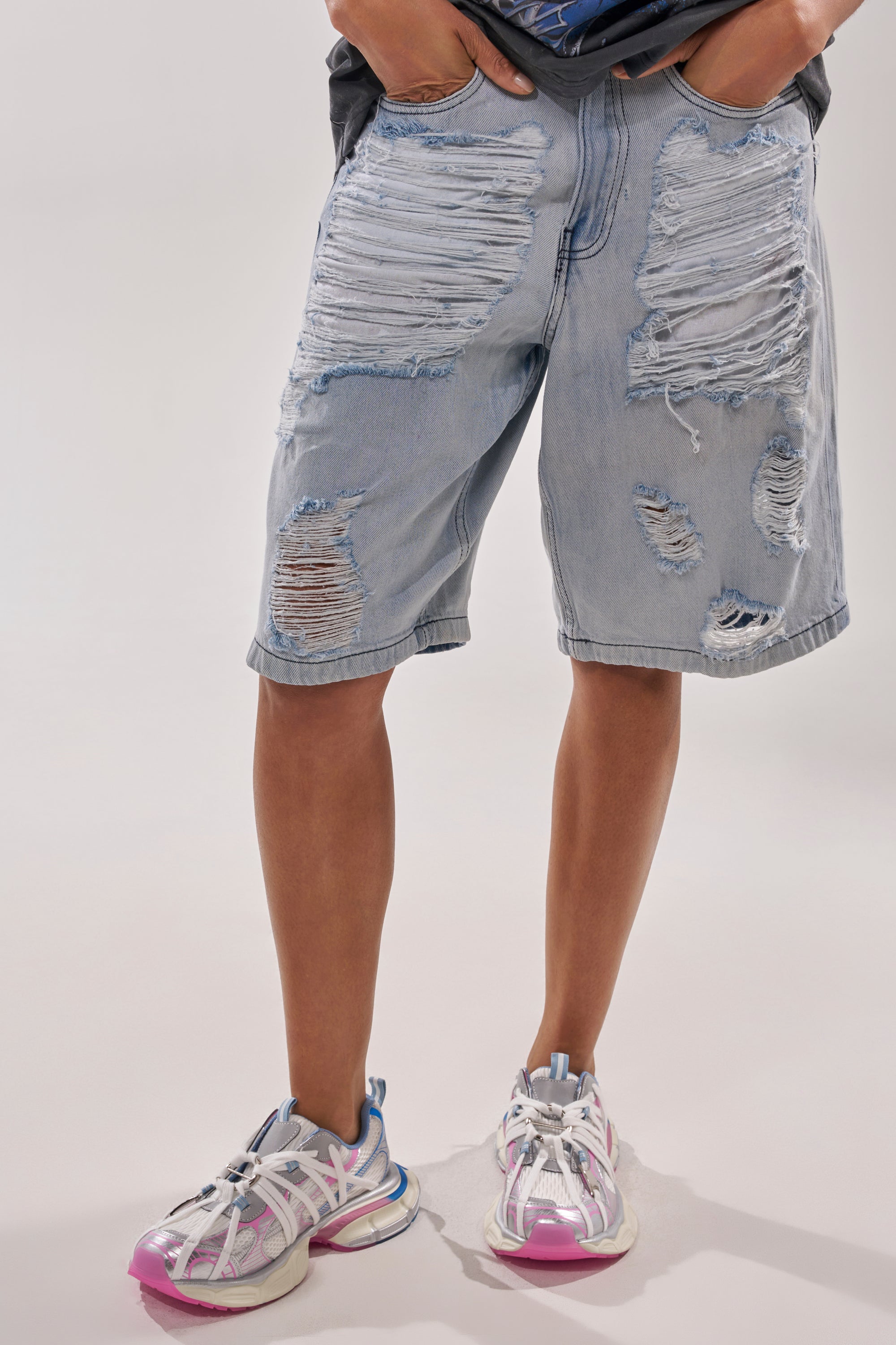 A person is wearing light blue, heavily distressed denim shorts with large rips, a dark t-shirt tucked in, and AZALEA WANG RANGLE PINK MULTI LACE SNEAKER. Only the lower body and part of the torso are visible. 3