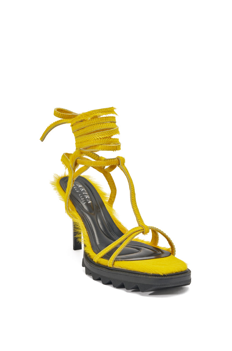 The AKIRA GOLD RAVZA Yellow Calf Hair Strap High Heel Stiletto Sandal features bright yellow fuzzy calf hair, lace-up straps, and a stiletto heel, shown against a white background. 4