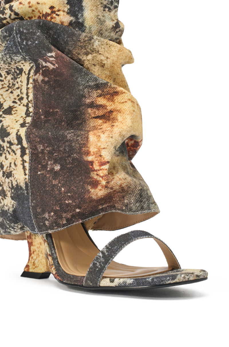 A close-up shows someone wearing the AZALEA WANG RAXA MULTI OPEN TOE BOOTIE, a slouchy wedge bootie with an open toe and a brown, black, and beige abstract pattern. The foot is partially visible in the sandal. 6