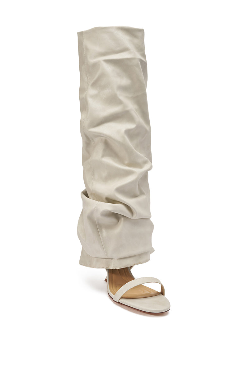 A person wears loose, ruched, light beige pants with the AZALEA WANG RAYLAN BONE GLADIATOR SANDAL—minimal knee-high wedges with a thin strap over the toes. 4