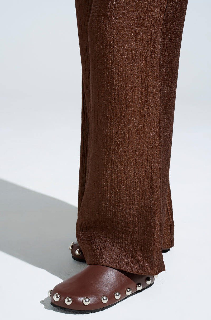 Close-up on AZALEA WANG RAYNE BROWN FLAT shoes, showcasing almond toes and metallic silver embellishments, paired with textured brown pants against a plain background. The focus is on the lower legs and feet.