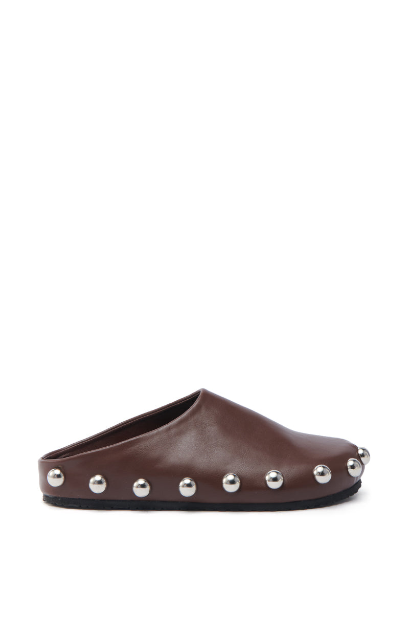 The AZALEA WANG RAYNE BROWN FLAT is a brown slip-on mule made from vegan leather, featuring an almond toe, flat sole, and silver metallic studs along the edge, all showcased on a plain white background.