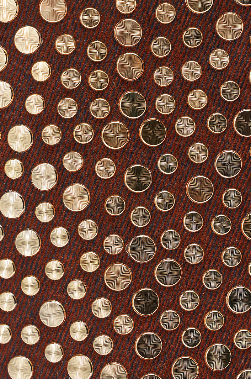 A close-up of the AKIRA GOLD RAYSSA BURNT ORANGE GOLD HARDWARE EMBELLISHED STILETTO SANDAL, showing gold stud accents and circular discs arranged on its faux suede, woven-textured reddish-brown surface. 7
