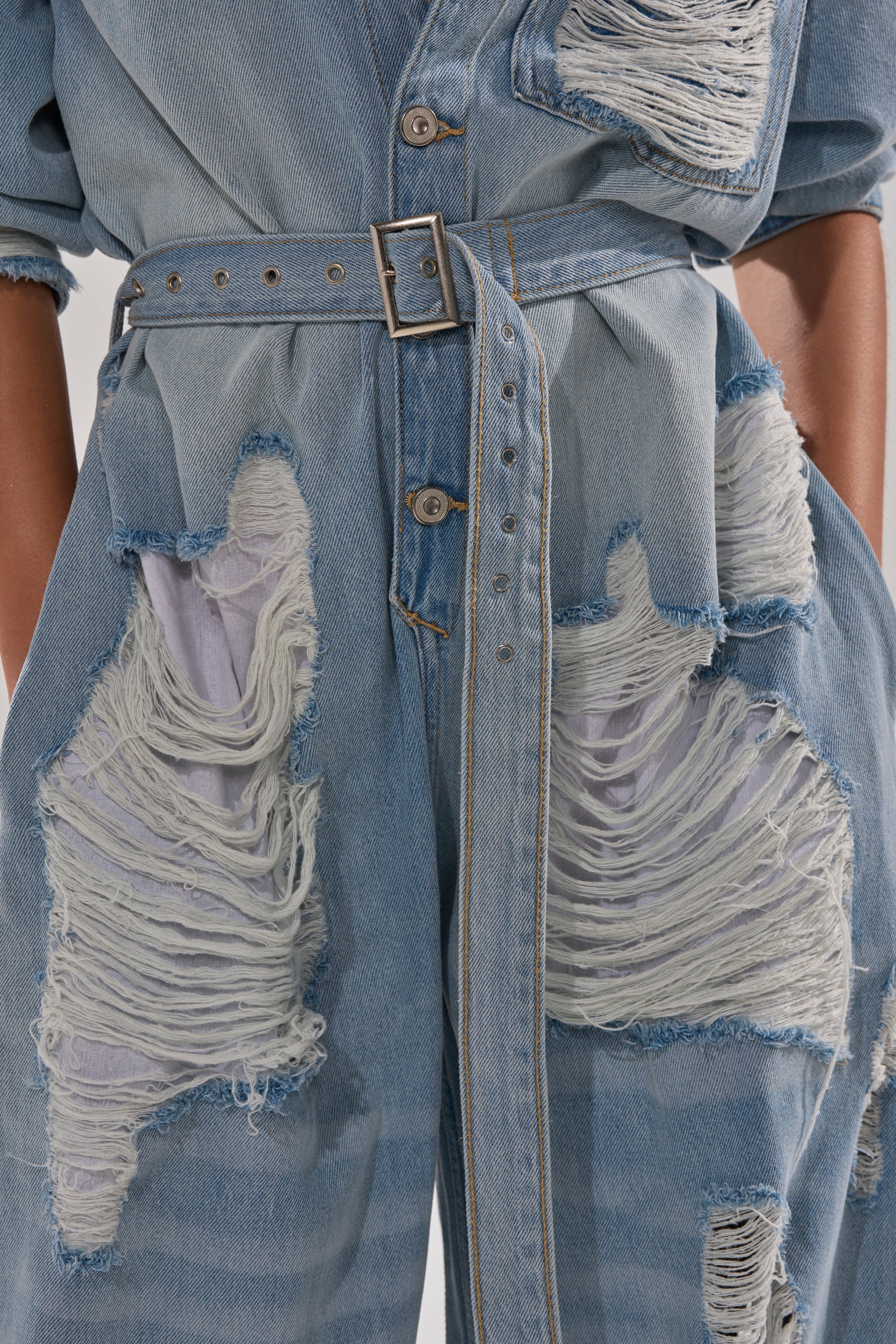 Close-up of a person wearing the NOT TODAY EXTREME OVERSIZED DISTRESSED DENIM JUMPSUIT, featuring large frayed holes, visible white inner fabric, and a matching adjustable waist belt.