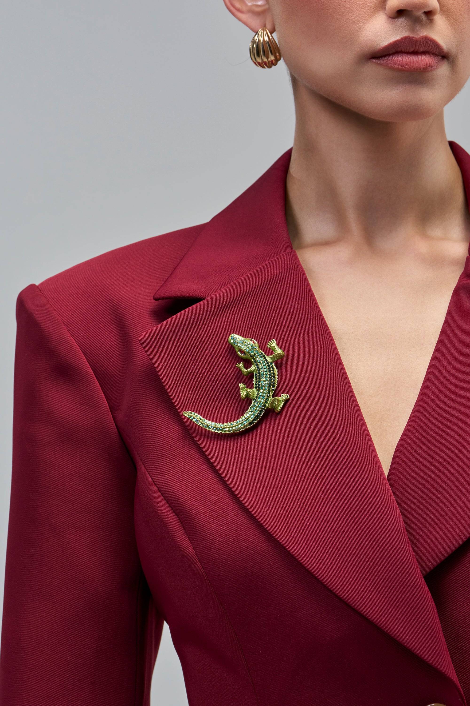 A green rhinestone BITE ME BROOCH IN GREEN reptile brooch pinned to the lapel of a red blazer.