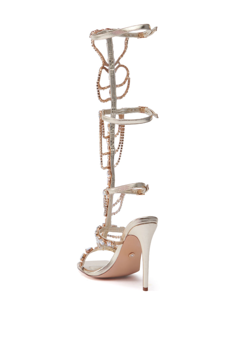 Introducing the AZALEA WANG REALEM GOLD EMBELLISHED GLADIATOR SANDAL: a dazzling pair of high-heeled sandals featuring a rhinestone-adorned, intricate knee-high lace-up design. With its shimmering bead embellishments and slender stiletto heel, this sandal offers an elegant and glamorous look.