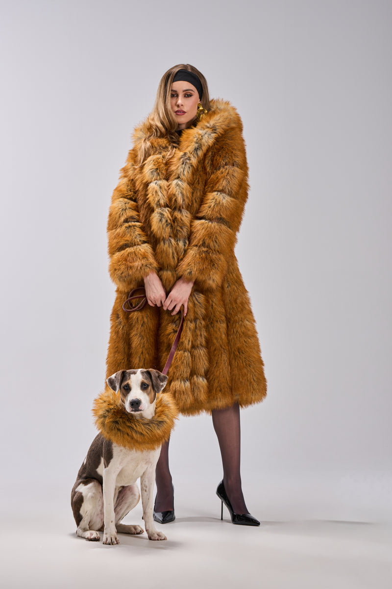 A woman in the OLD MONEY FAUX FUR COAT stands with her dog, who sports a matching furry collar. Both face forward against a plain light gray background, highlighting their coordinated luxury outerwear.