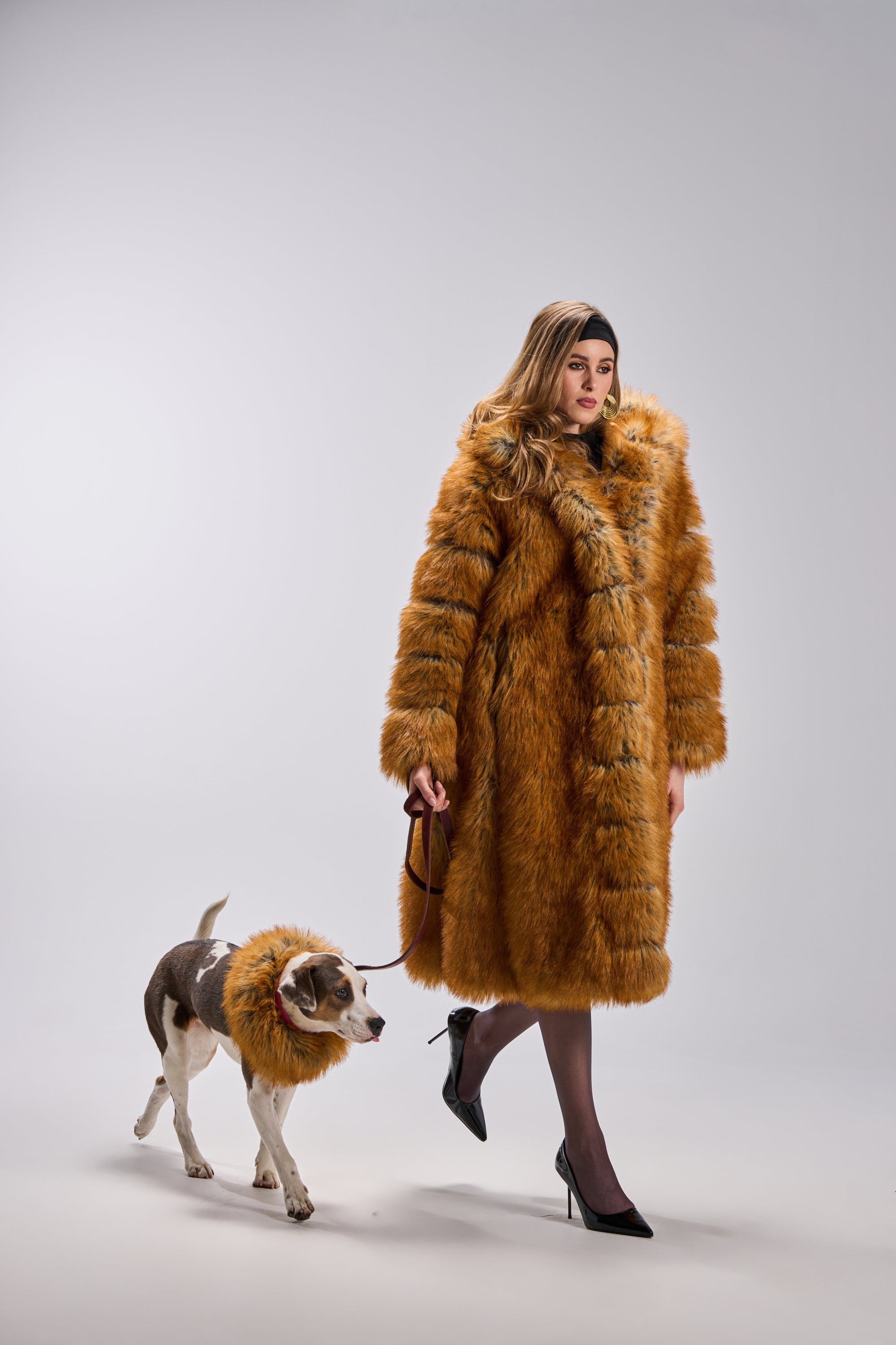 A woman in an OLD MONEY FAUX FUR COAT walks her dog, both adorned in matching faux fur, against a simple backdrop—highlighting their stylish coordination and the sophisticated appeal of this luxurious outerwear.